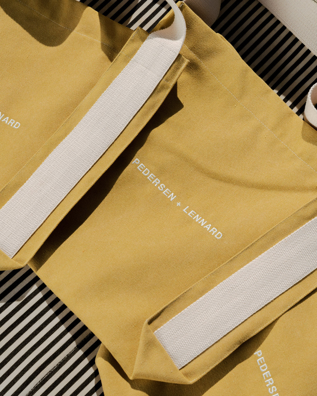 Mustard yellow bag with white straps on a black and white striped background