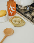 Brass spoon rest, wooden spoon and a lemon next to a gas stove top