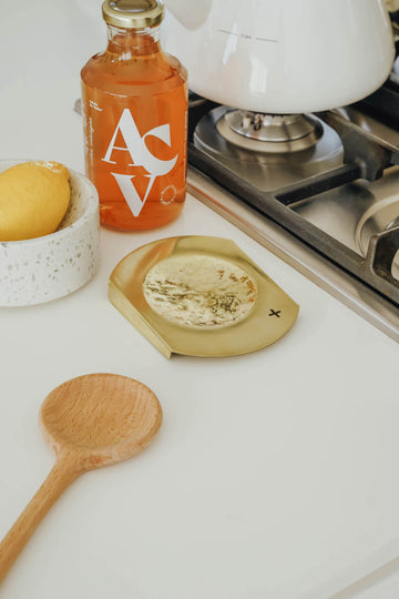 Brass spoon rest, wooden spoon and a lemon next to a gas stove top